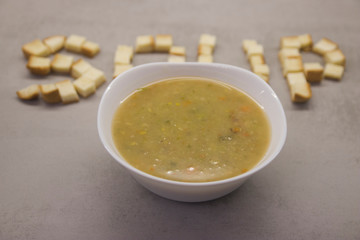 word SOUP made of square toast ryados with a round bowl of soup on a gray kitchen table with texture top view