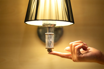 Hand of person is turning on or turning off the antique bedroom 's head lamp by pushing switch at the bottom. Close up and selective focus photo. Energy saving concept.