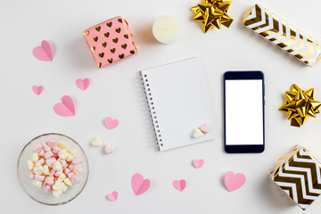 Composition for Valentine's Day February 14th. A gentle composition of pink hearts made of paper, gifts, a phone and a heart-shaped marshmallow on a white background. Flat lay, top view, copy space.