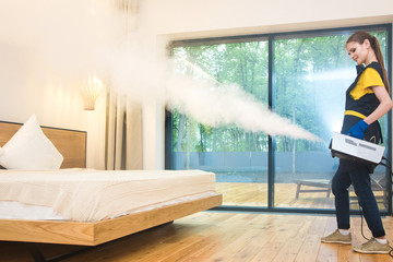 professional cleaning service. woman in uniform and gloves does the cleaning in a cottage. treatment, disinfection of the apartment with hot steam from odors and parasites, bed bugs