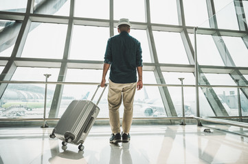 Fototapeta na wymiar A male traveler wearing a gray hat Preparing to travel He has a trolley bag He stands at a large airport for traveling around the world.