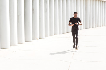 Athletic young afroamerican man running on the promenade. Black Male runner sprinting outdoors. Healthy lifestyle concept.