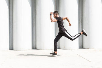 Athletic young afroamerican man running on the promenade. Black Male runner sprinting outdoors. Healthy lifestyle concept.