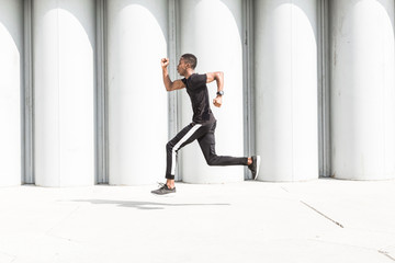 Athletic young afroamerican man running on the promenade. Black Male runner sprinting outdoors. Healthy lifestyle concept.