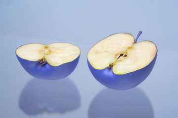 a blue Apple cut in half on a light blue background. The two halves of the fruit.