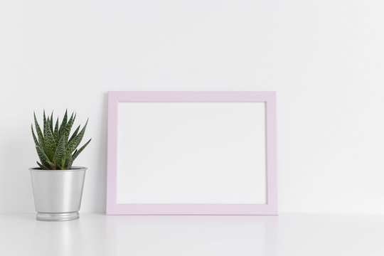 Pink frame mockup with a cactus in a pot on a white table.Landscape orientation.