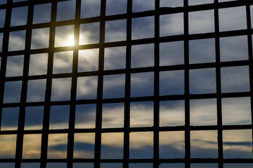 Look through the bars at the sky. Pale sunlight breaking through the dark clouds. To be imprisoned or behind the bars. To lose freedom concept. Hopelessness and loneliness.