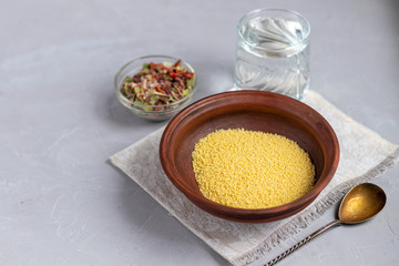 Raw couscous groats, a glass of clean, hot water and dry vegetables.