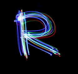 Long exposure photograph of a letter r in neon colour in an abstract swirl, parallel lines pattern against a black background. Light painting photography.