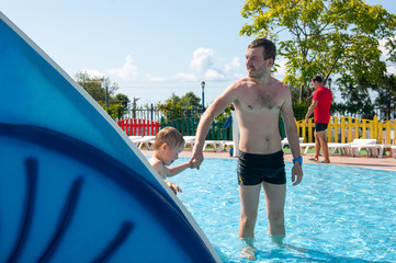 A happy three-year-old boy is playing catch-up with his father in the outdoor pool of a water park. Summer, vacation, vacation, sun, south, tan, family, parent, son, boy, young man, healthy lifestyle