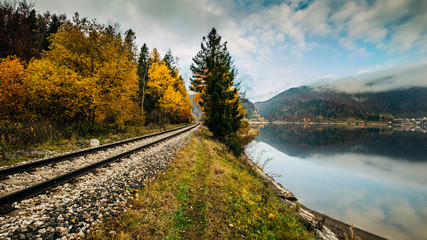 railway trail through mountains near lake, autumn colours