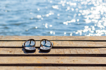 Pair of flip flops on the wooden dock and scenery of lake river at natural background.