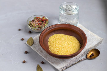 Raw couscous groats, a glass of clean, hot water and dry vegetables.