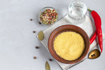 Raw couscous groats, a glass of clean, hot water and dry vegetables.