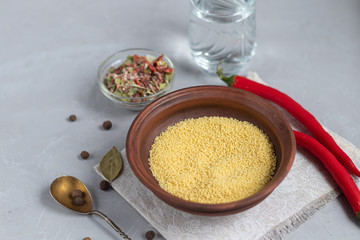 Raw couscous groats, a glass of clean, hot water and dry vegetables.