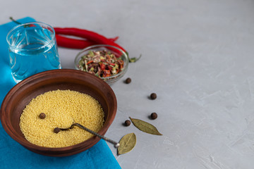 Raw couscous groats, a glass of clean, hot water and dry vegetables.
