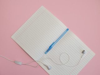 notebook in a line with a pen for writing and headphones on a pink background