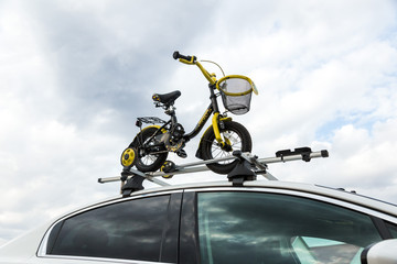 Bicycle transport - a children's bicycle on the roof of a car against the sky in a special mount for cycling. The decision to transport large loads and travel by car