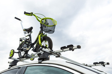 Bicycle transport - a children's bicycle on the roof of a car against the sky in a special mount for cycling. The decision to transport large loads and travel by car