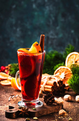 Christmas mulled red wine with spices and fruits in tall glass on wooden rustic table. Traditional Christmas hot drink in festive table setting