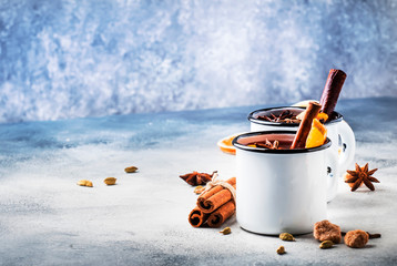 Mulled wine in white metal mugs with cinnamon, spices and orange on concrete background, traditional drink on winter holiday. Copy space for text