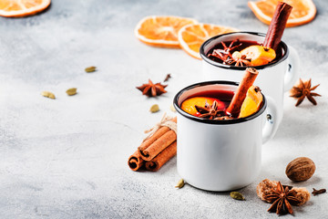 Mulled wine in white metal mugs with cinnamon, spices and orange on concrete background,...