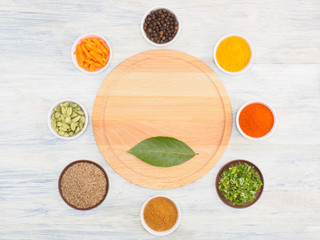Obraz na płótnie Canvas Round kitchen cutting board and ingredients for cooking: black pepper, turmeric, chili, green grass, masala, cumin (jeera), cardamom, carrot. Healthy eating concept