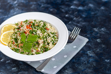 Tabbouleh  salad in a round plate on a wooden background. salad in a white plate on a dark blue, trendy background 2020.