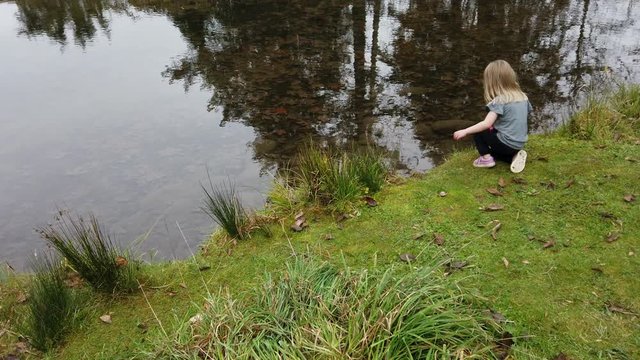 A young girl walks to a stream at woodland setting nature play puts a hand in the river slow motion