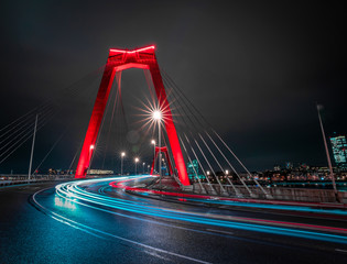 Obraz premium Light trails of traffic at the Willemsbrug in Rotterdam. Beautiful red bridge. Landmark of the skyline in Rotterdam, long exposure shot. 