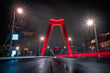 Fototapeta na wymiar Light trails of traffic at the Willemsbrug in Rotterdam. Beautiful red bridge. Landmark of the skyline in Rotterdam, long exposure shot. 