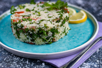 Tabbouleh  salad in a round plate on a wooden background. salad in a round plate on a dark blue, trendy background 2020.