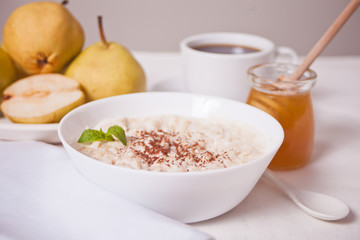 Oatmeal porridge in the white bowl, a bowl of pears, honey and cup of coffee on the background. Health breakfast. Close up.