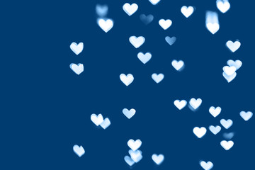 Trendy classic blue colored festive background with white heart bokeh. Christmas, New Year and Valentine's day design. Color of the year trend concept 2020