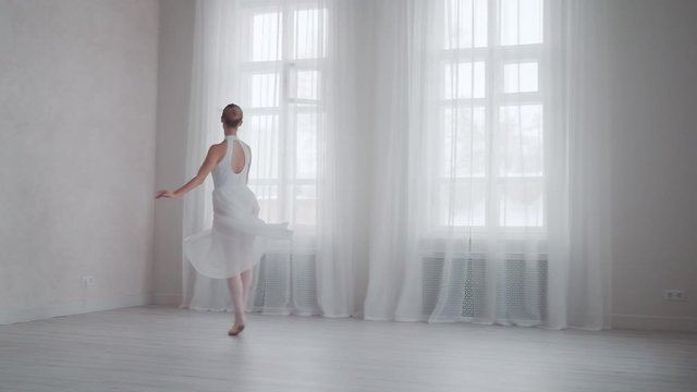 ballerina is spinning on tiptoe in a snow-white dress in a bright studio on the background of large windows