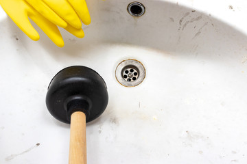 Blocked sewer, clogged wash bowl, basin drain, yellow rubber gloves and a plunger near in the bathroom at home