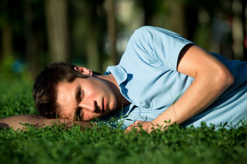 Naklejka na ściany i meble Young man in casual clothing lying on green grass and looking at camera