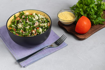 Tabbouleh  salad in a round plate on a light gray background under concrete.