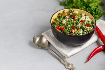 Tabule salad in a round plate on a light gray background under concrete.