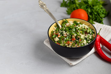 Tabule salad in a round plate on a light gray background under concrete.