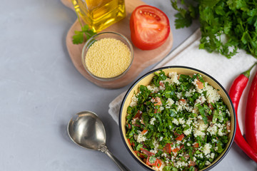 Tabbouleh  salad in a round plate on a light gray background under concrete.