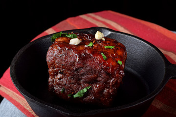 Fried pork loin piece with wine glazing in the cast iron pan against the black background