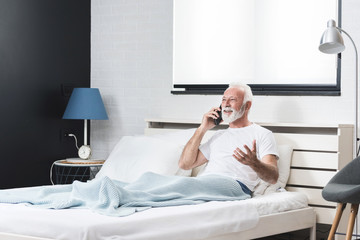 Senior man using mobile phone in bed in his room