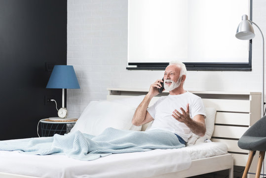Senior man using mobile phone in bed in his room - Powered by Adobe