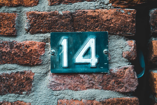 House number 14 on red brick wall with numbers fourteen on blue metal plate enameled