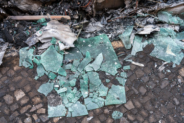 Broken windows lying on the road in front of a burnt-out car.