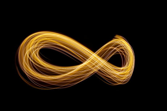 Long exposure photograph of an infinity loop in gold neon colour in an abstract swirl, parallel lines pattern against a black background. Light painting photography.