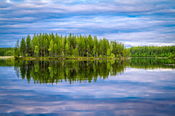 Karelian lakes at sunset and sunrise. Clouds and trees are reflected in the lake