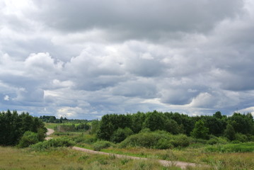 Fototapeta na wymiar summer landscape with sandy road, fields on hills and Cumulus clouds