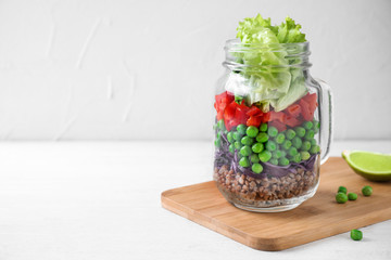 Healthy salad in glass jar on white wooden table. Space for text